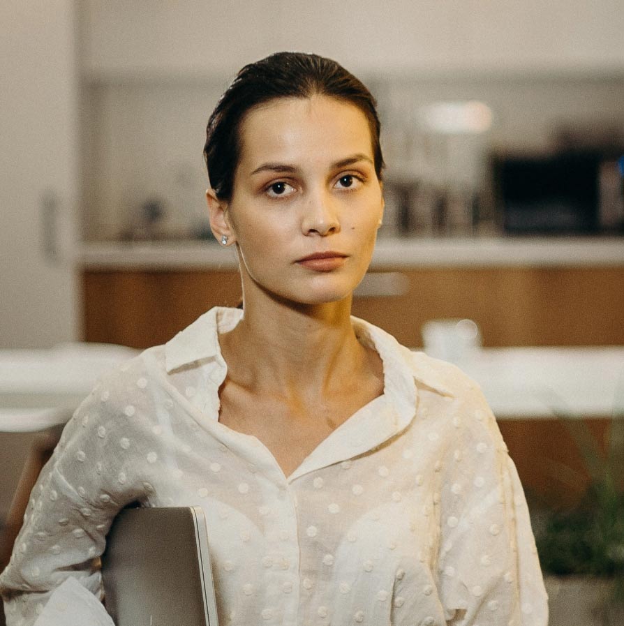 A woman with dark hair pulled back looking directly at the camera with a neutral expression