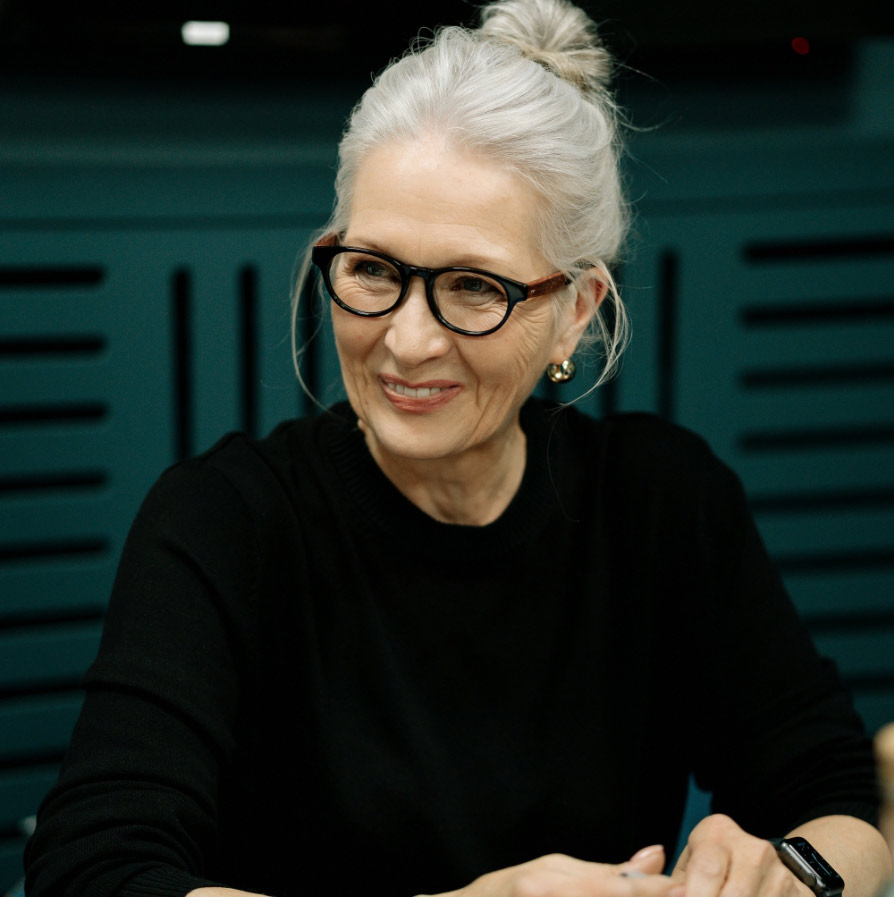 An older woman with black sweater smiles while looking to the side.