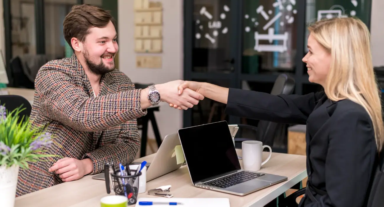 A man in a patterned blazer and a woman in a black jacket shaking hands