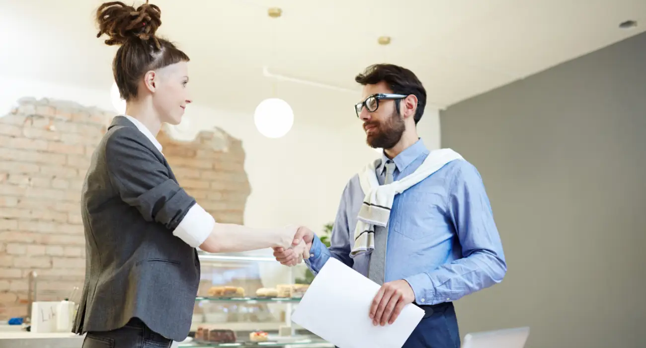 A woman with a high, styled bun and a grey blazer shaking hands with a man